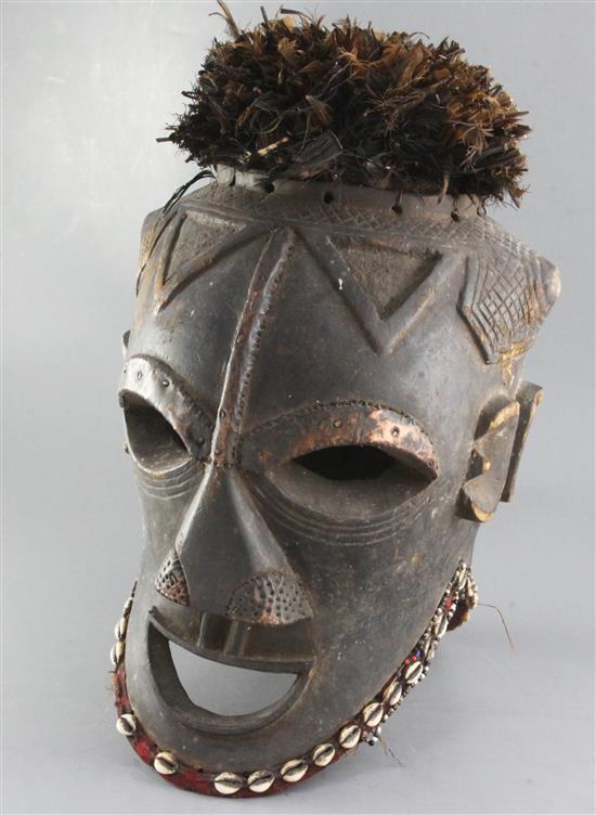 A large West African carved wood Janus helmet mask, decorated with cowrie shells and feathers, height 49cm
